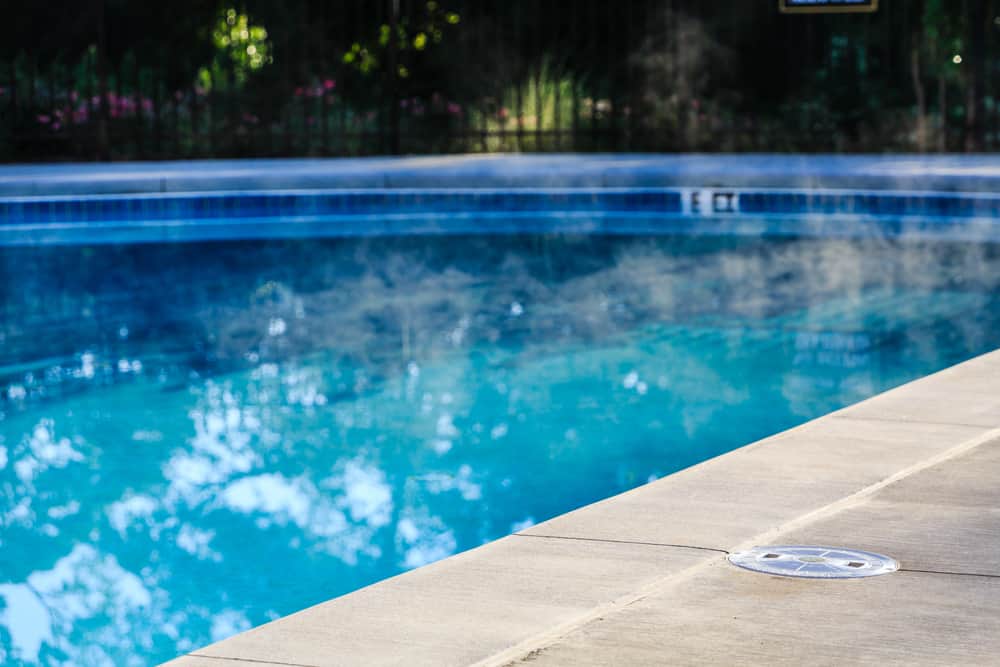 A steaming swimming pool with a concrete edge - What Technologies are Available to Warm My Pool?