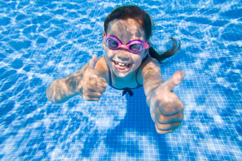 Cheerful little girl playing under water in pool - The Dos and Don'ts of Pool Heating